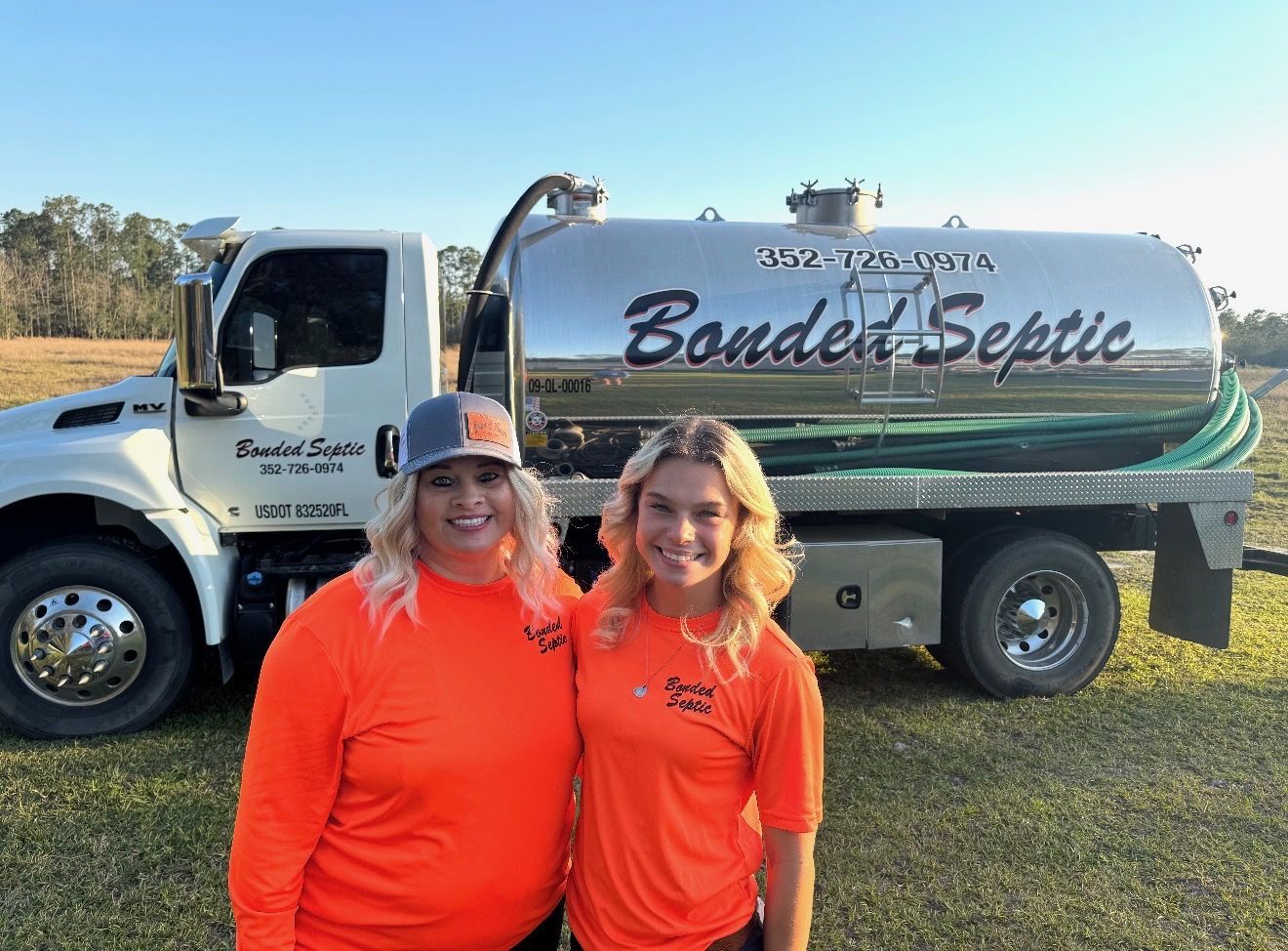 Bonded Septic Tank family team in orange company shirts standing in front of a septic pump truck